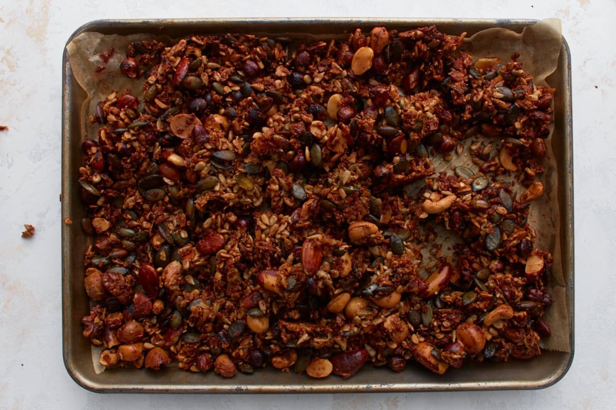 Freshly baked keto granola on a parchment-lined baking sheet, showing golden brown clusters of nuts and seeds after cooling.
