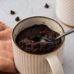 Spoon scooping a fudgy almond flour chocolate mug cake from a ceramic mug with melted chocolate chips inside