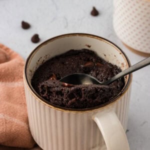 Spoon scooping a fudgy almond flour chocolate mug cake from a ceramic mug with melted chocolate chips inside