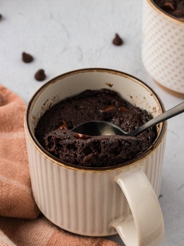 Spoon scooping a fudgy almond flour chocolate mug cake from a ceramic mug with melted chocolate chips inside