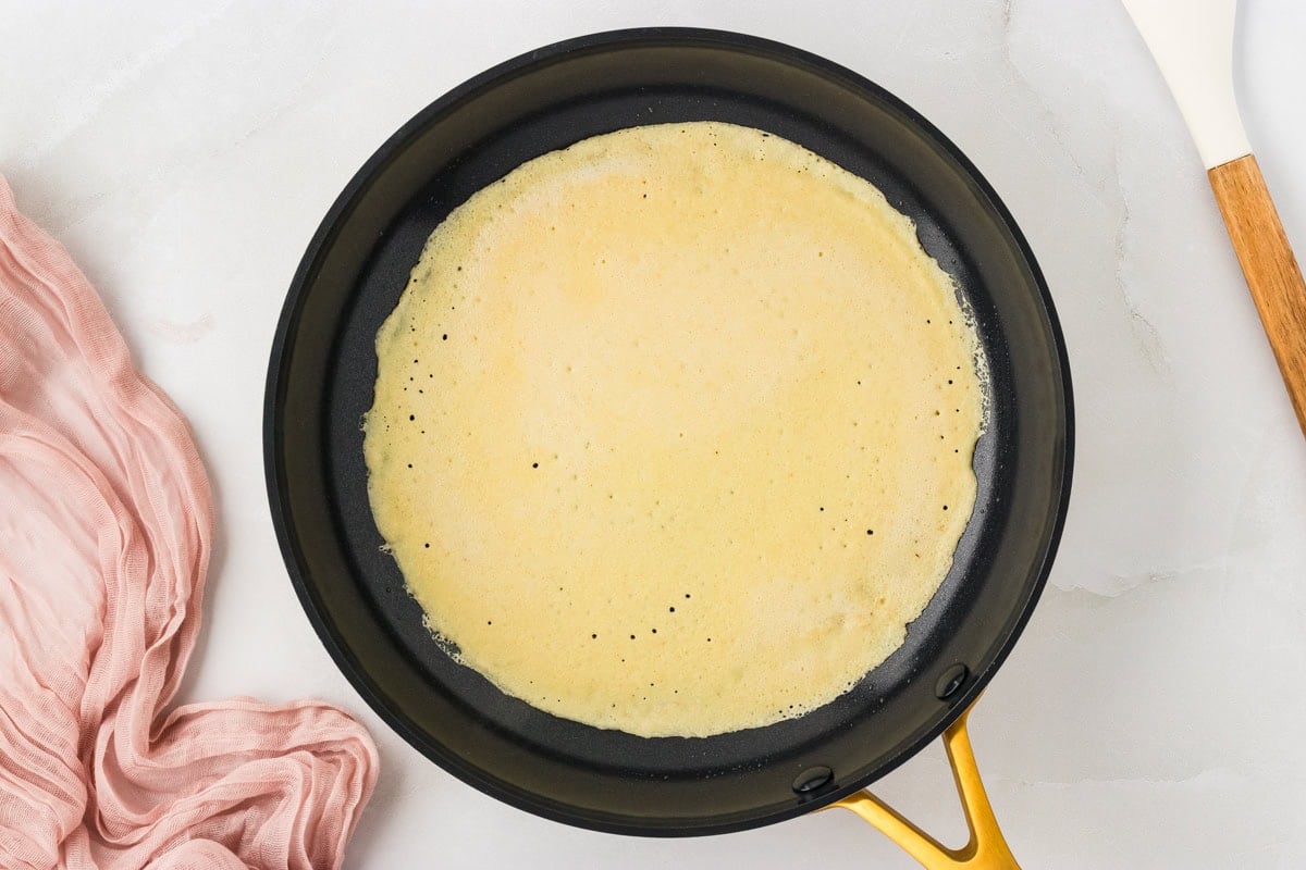 Thin almond flour crepe batter cooking in a nonstick pan before flipping