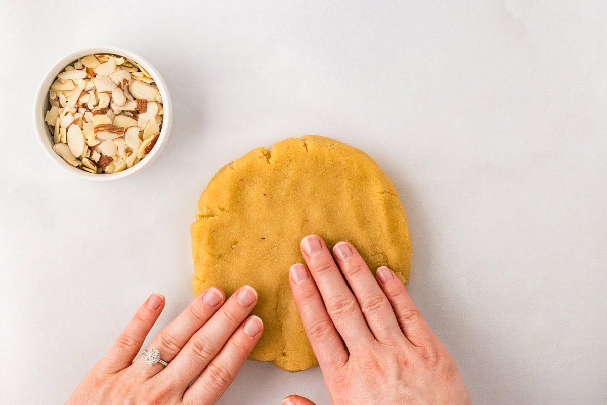 Hands pressing almond flour scone dough into thick disc before cutting