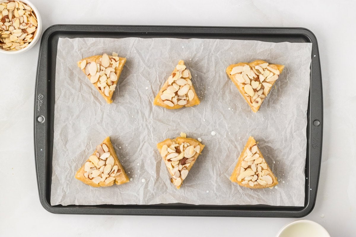 Unbaked almond flour scones topped with sliced almonds on parchment lined baking sheet