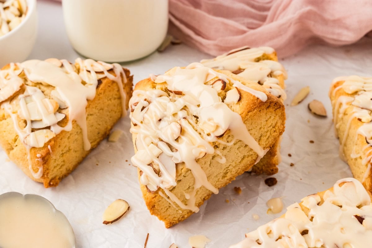 Almond flour scones drizzled with icing and topped with sliced almonds on parchment paper