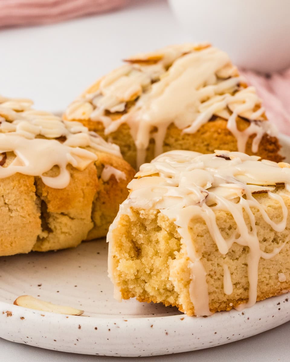 Close-up of almond flour scone with vanilla icing drizzle and sliced almonds showing soft crumb