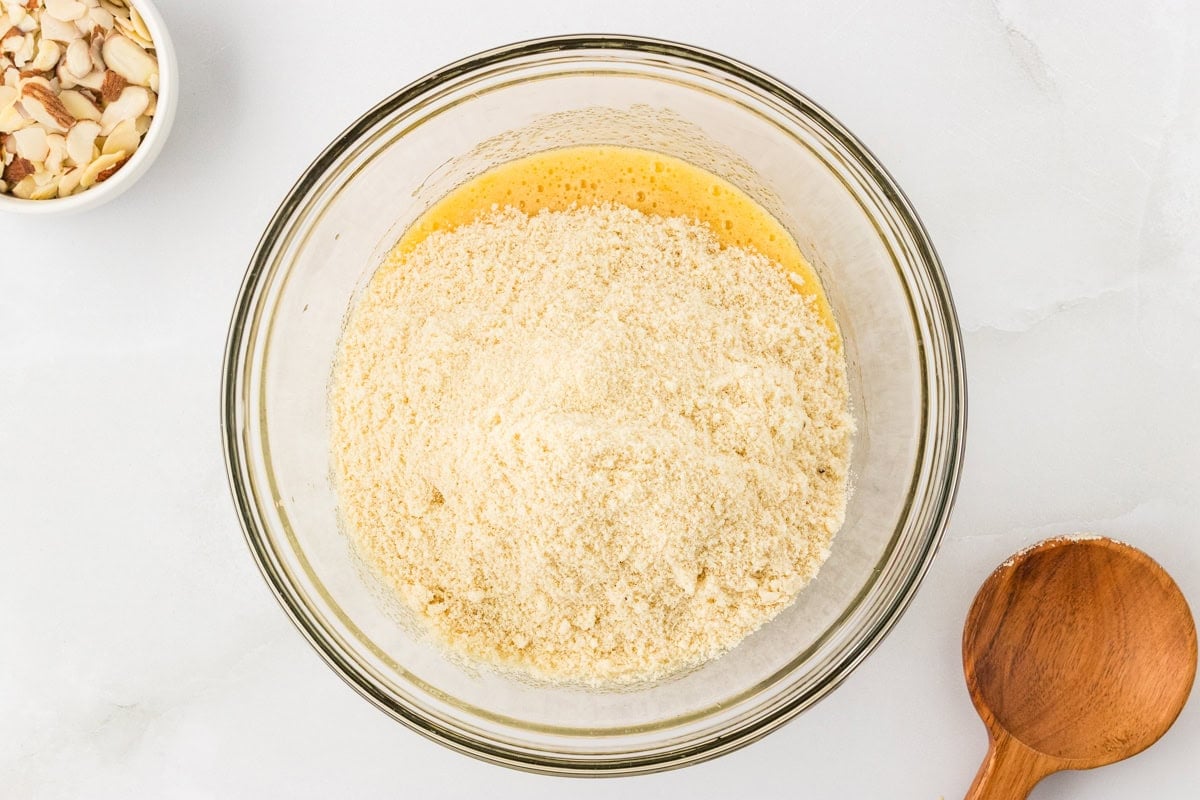 Almond flour mixture added to wet ingredients in glass mixing bowl