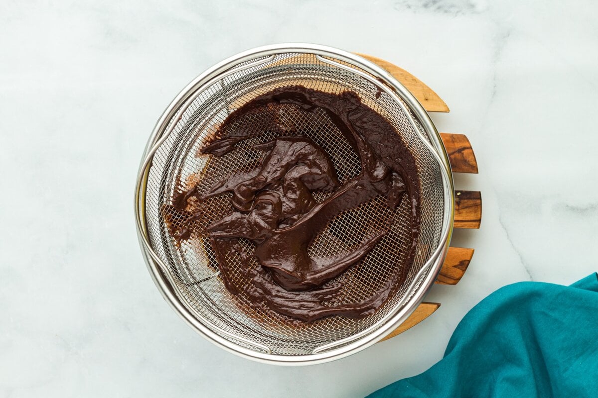 Chocolate custard being strained through a fine mesh strainer to remove lumps.