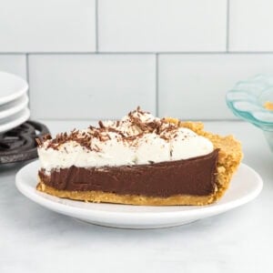 Slice of gluten-free chocolate pie with creamy chocolate custard filling, graham cracker crust, and whipped cream topping on a white plate.
