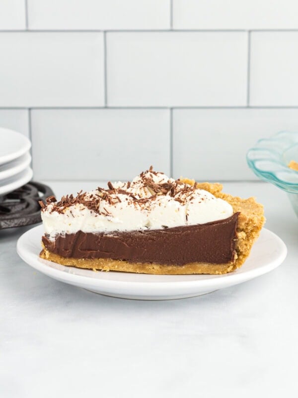 Slice of gluten-free chocolate pie with creamy chocolate custard filling, graham cracker crust, and whipped cream topping on a white plate.