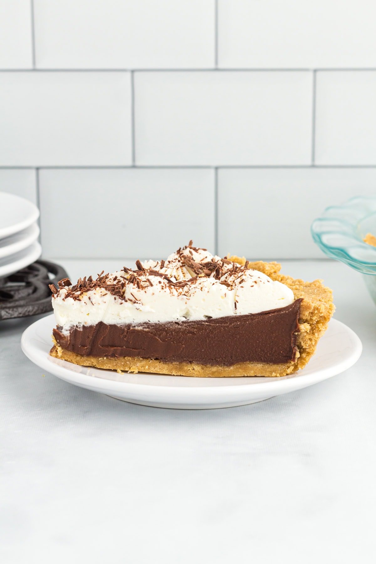 Slice of gluten-free chocolate pie with creamy chocolate custard filling, graham cracker crust, and whipped cream topping on a white plate.