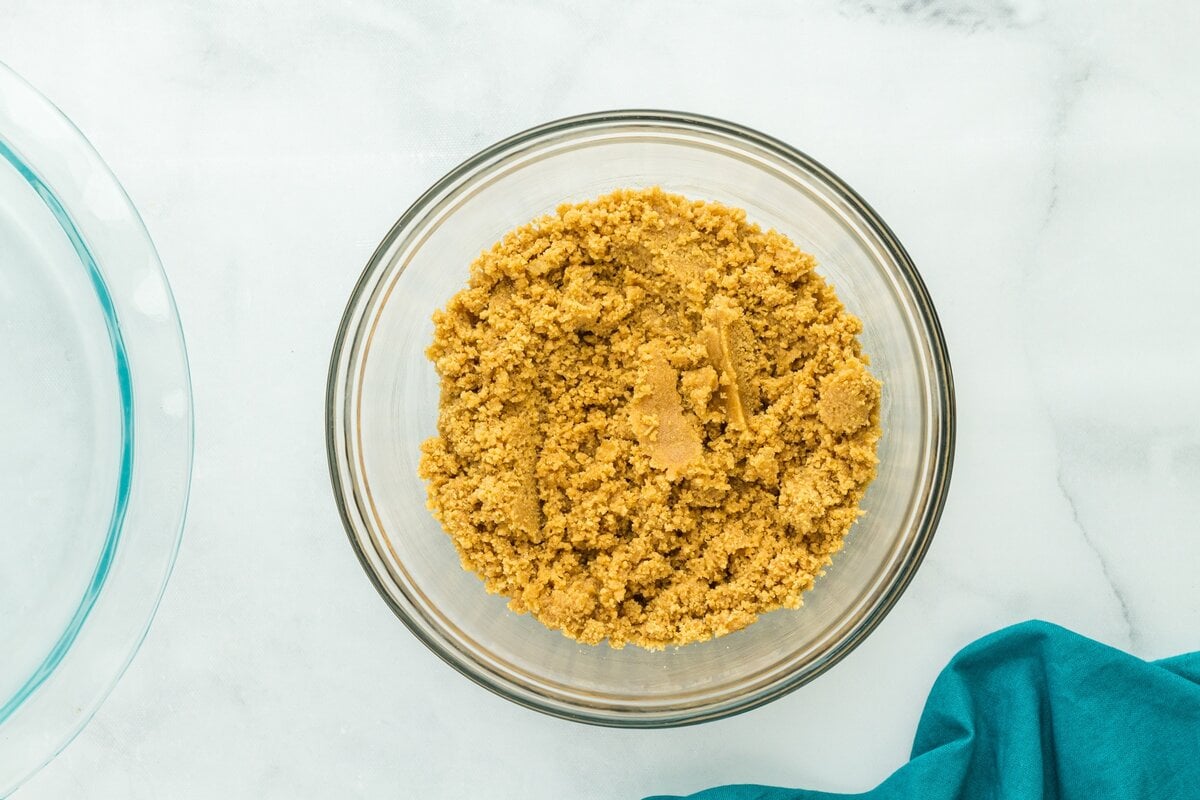 Gluten-free graham cracker crumbs mixed with melted butter and sugar in a glass bowl for pie crust.
