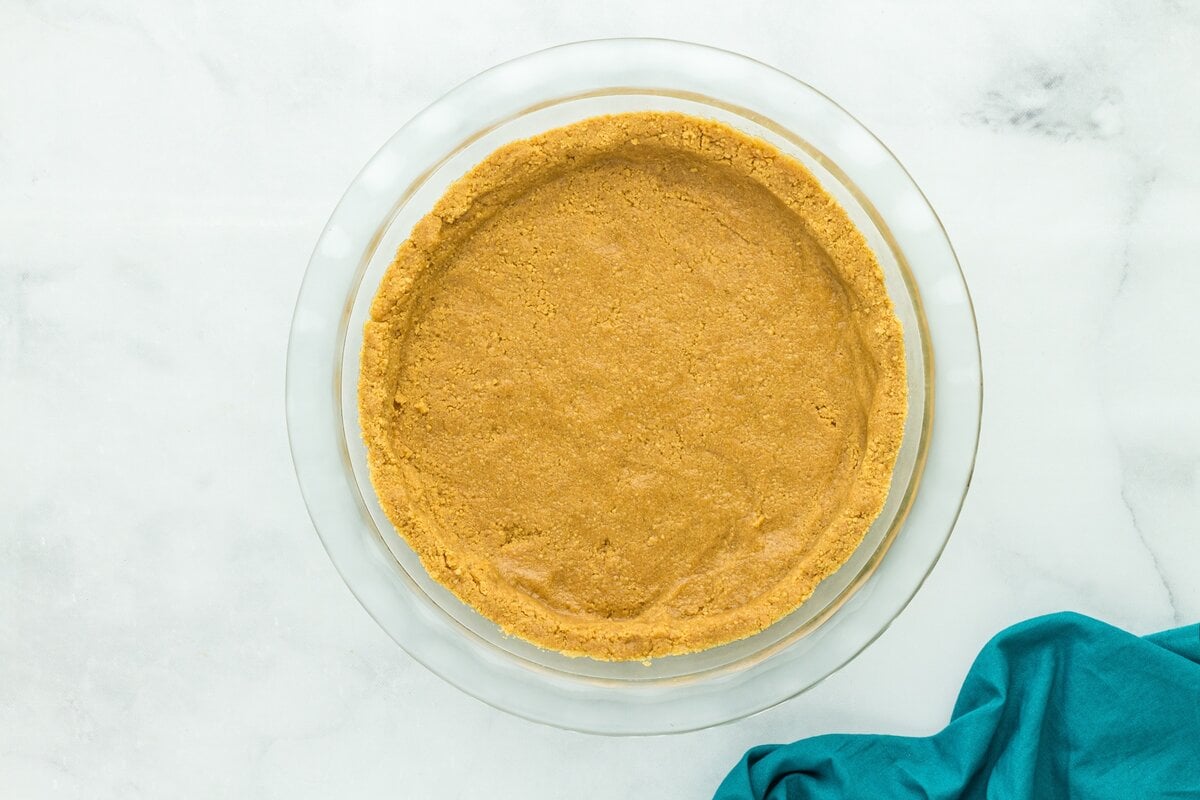 Gluten-free graham cracker crust pressed evenly into a glass pie plate before baking.