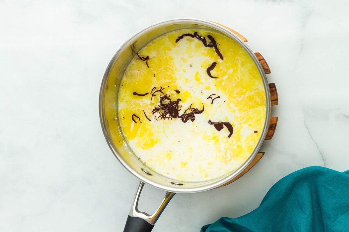 Chocolate custard mixture cooking in a saucepan on the stovetop while being whisked.