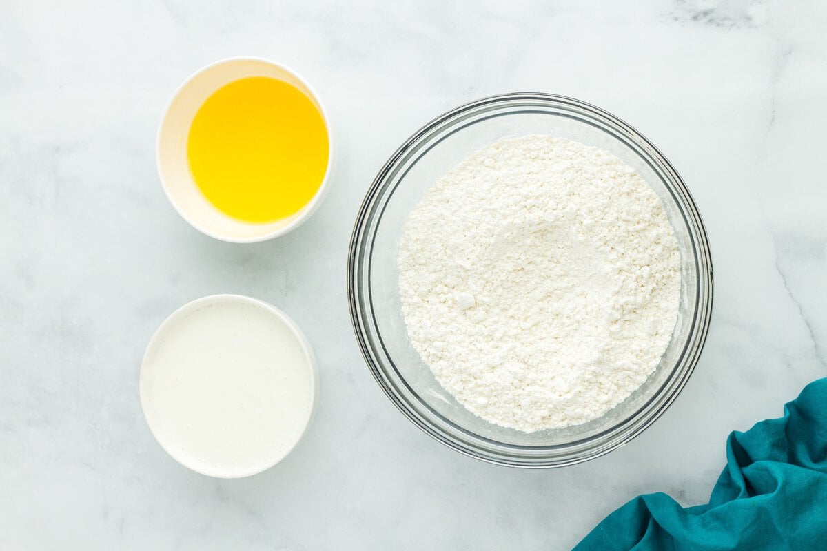 Bowl of gluten free flour beside melted butter and buttermilk on a marble surface.