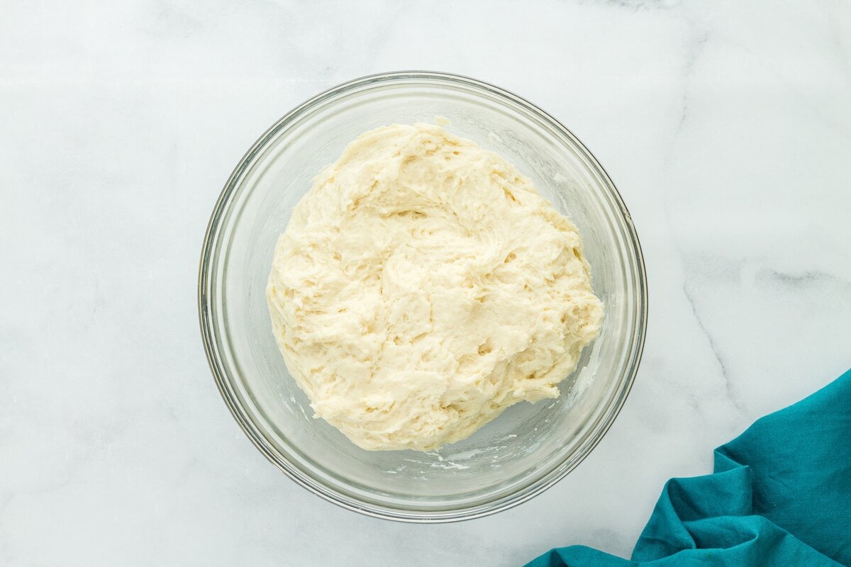 Sticky gluten free dough partially mixed in a glass bowl, showing rough, shaggy texture.