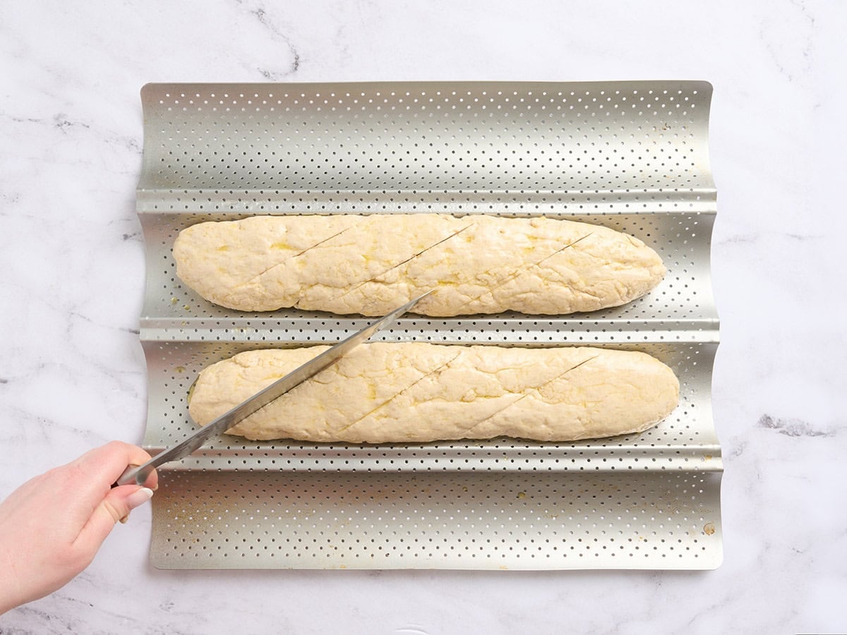 Two shaped gluten-free baguettes placed on a perforated baguette pan and brushed lightly with oil.