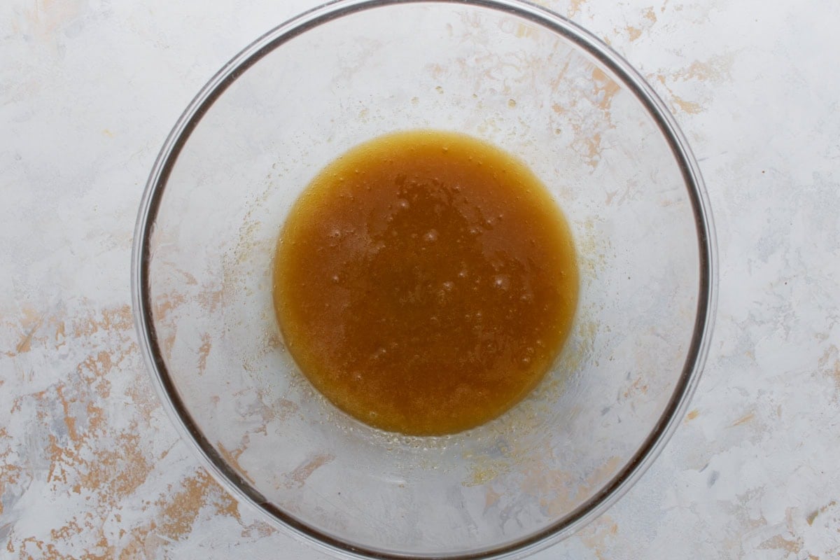 Melted butter and sugars combined in a clear glass mixing bowl