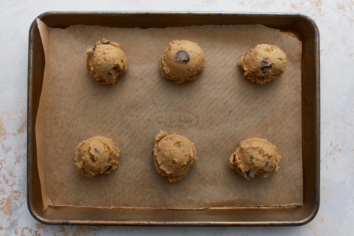 Scoops of buckwheat chocolate chip cookie dough portioned onto a parchment lined baking sheet before baking