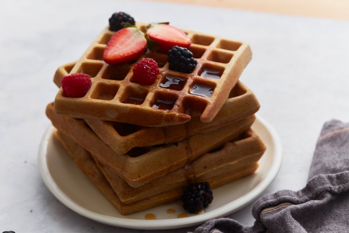 Tall stack of homemade buckwheat waffles with berries and syrup on a white plate