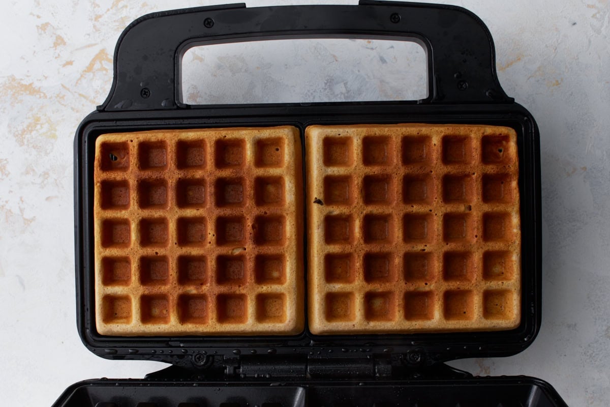 Golden brown buckwheat waffles cooking in an open waffle maker