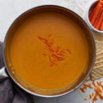 Gluten-free beer cheese dip finished in saucepan with shredded cheddar on top, served with crackers and carrots