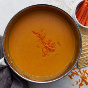 Gluten-free beer cheese dip finished in saucepan with shredded cheddar on top, served with crackers and carrots