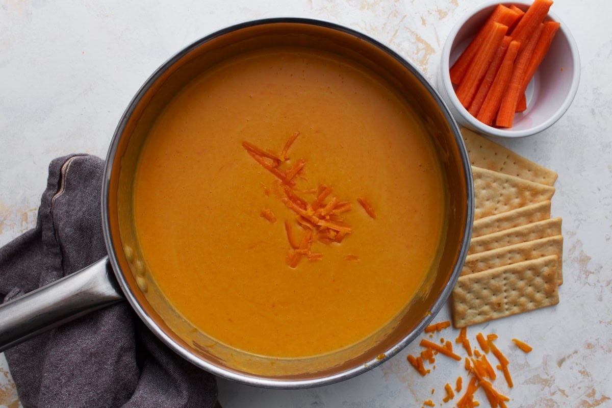 finished gluten-free beer cheese sauce in a saucepan with carrots and crackers nearby for dipping