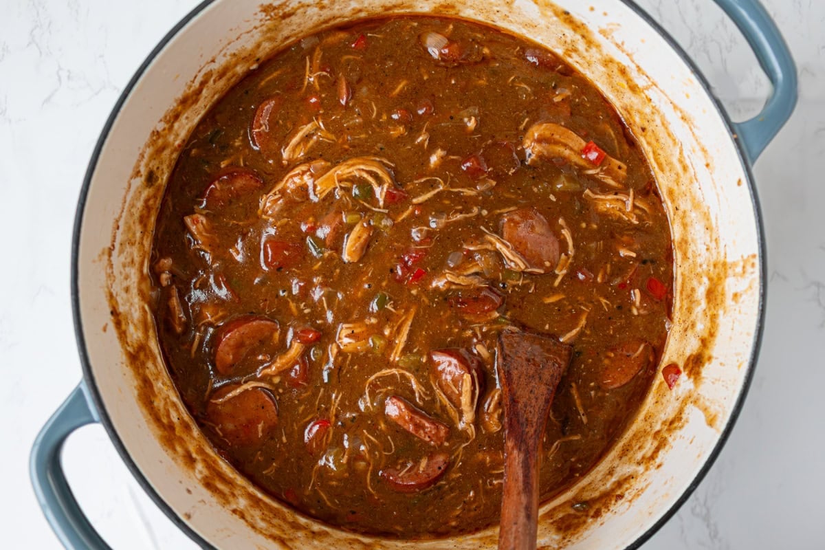 Gluten free chicken and sausage gumbo simmering and thickening in a Dutch oven with deep brown broth.