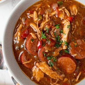 Bowl of gluten free chicken and sausage gumbo garnished with fresh parsley showing rich broth, shredded chicken, and sliced andouille.
