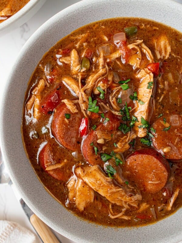 Bowl of gluten free chicken and sausage gumbo garnished with fresh parsley showing rich broth, shredded chicken, and sliced andouille.