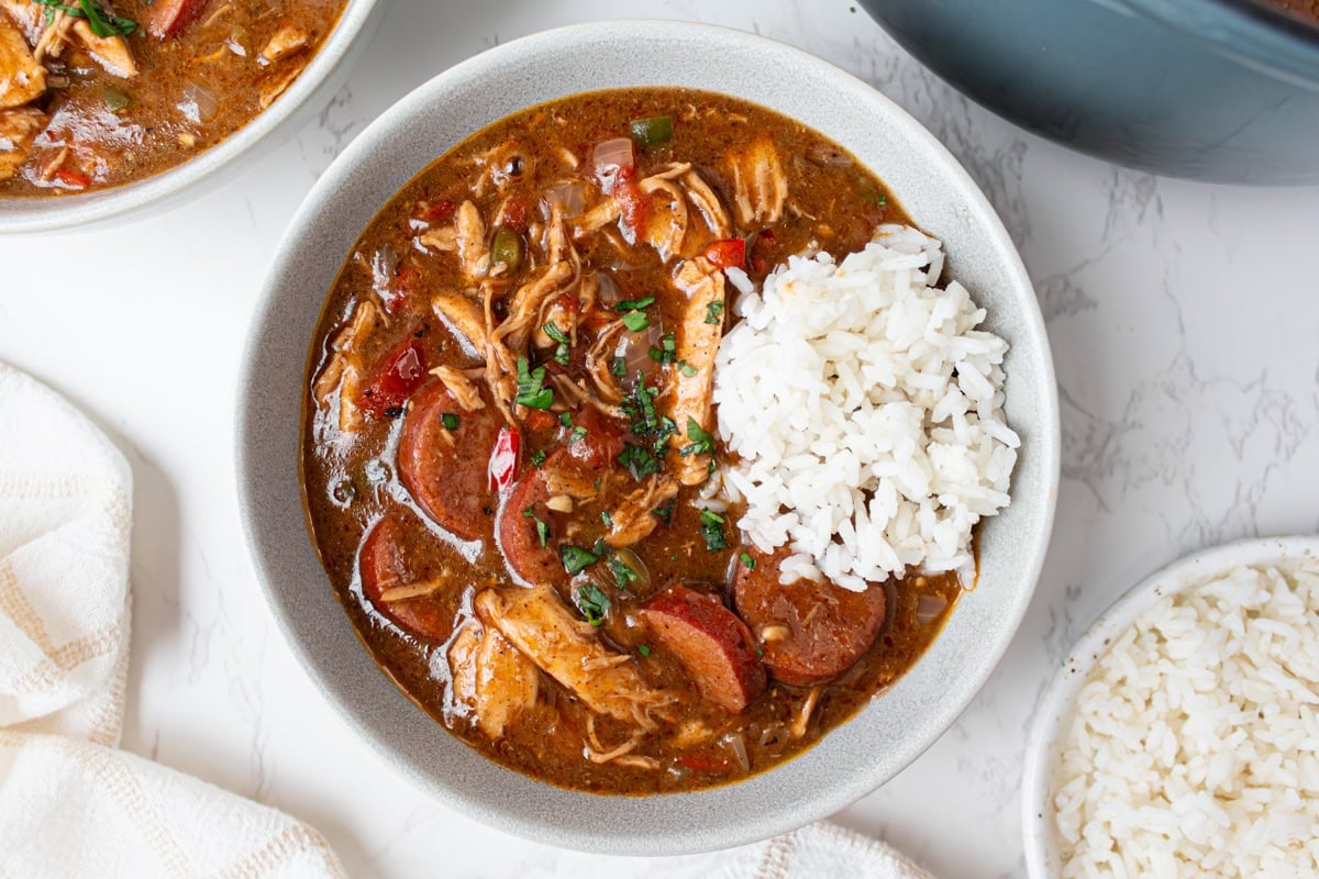Bowl of gluten free gumbo served with white rice and fresh parsley garnish on top.