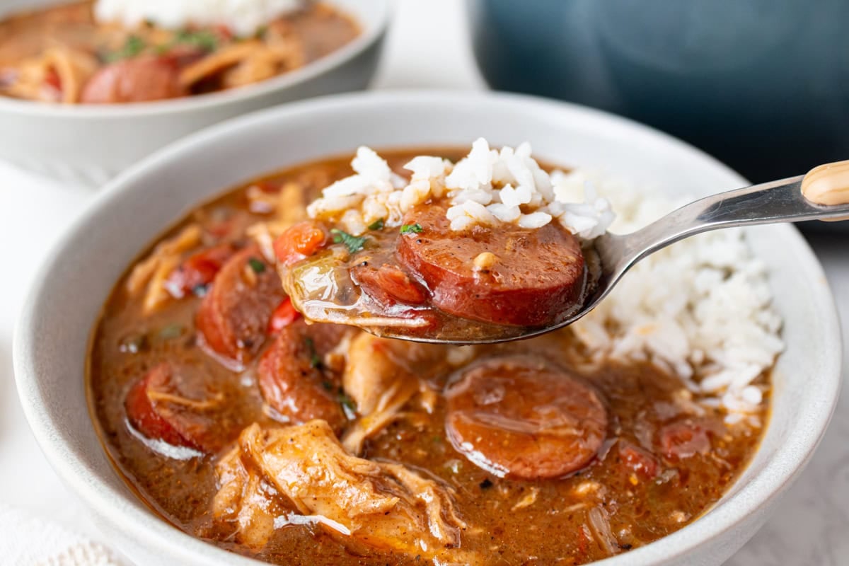 Spoonful of chicken, sausage, vegetables, and rice lifted from a bowl of rich gluten free gumbo.