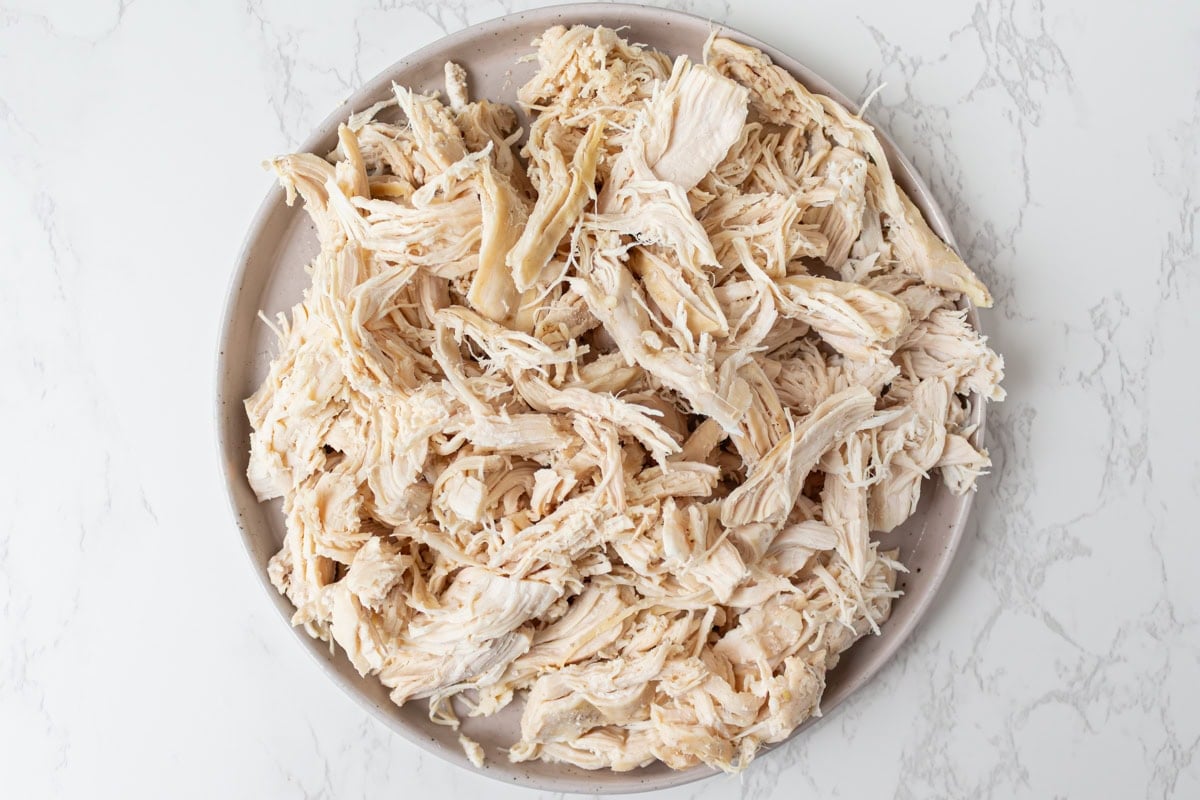 Shredded chicken piled on a plate after being pulled apart with forks.