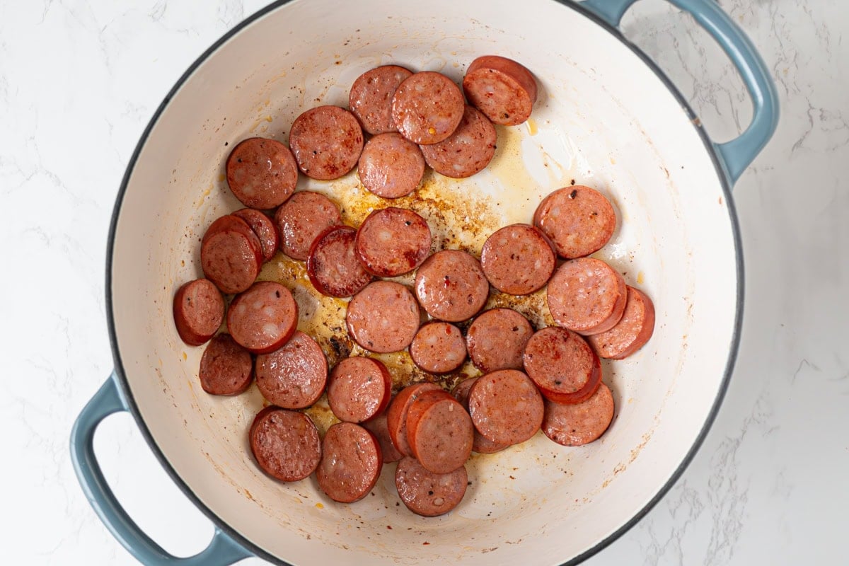 Andouille sausage slices browning in a Dutch oven with flavorful drippings left in the pan.