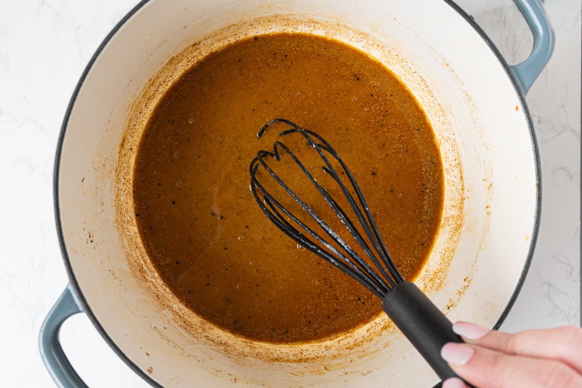 Gumbo base being whisked with Cajun seasoning into the roux creating a thick, dark, flavorful mixture.