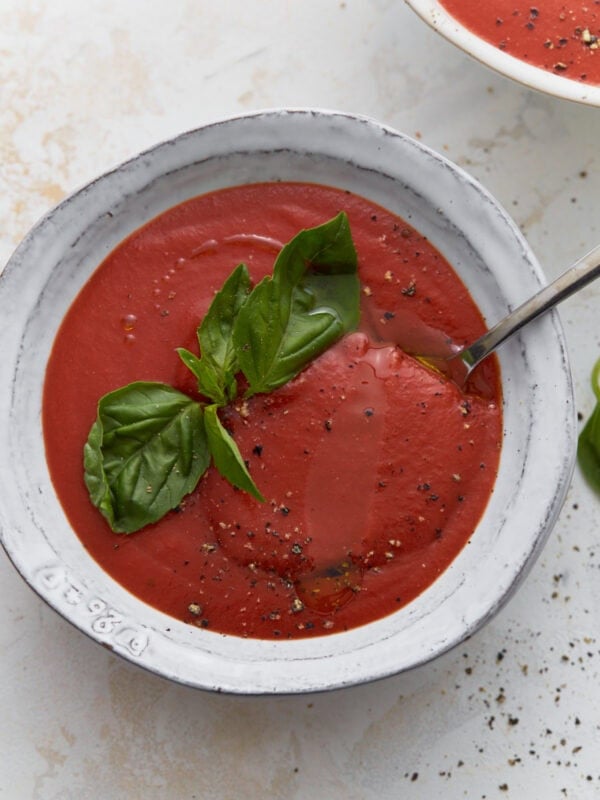 Gluten-free tomato soup in white bowl topped with fresh basil, cracked black pepper, and olive oil drizzle