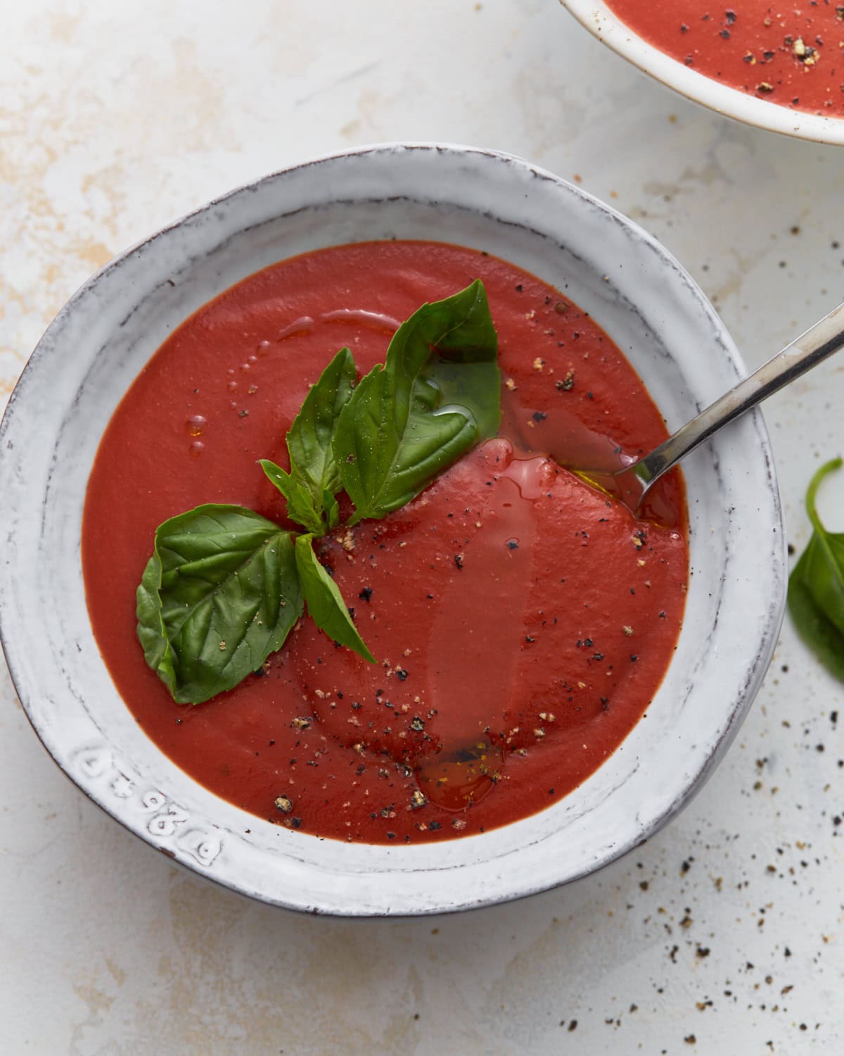 Gluten-free tomato soup in white bowl topped with fresh basil, cracked black pepper, and olive oil drizzle