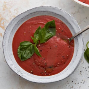 Close-up of gluten-free tomato soup with basil garnish and spoon in bowl