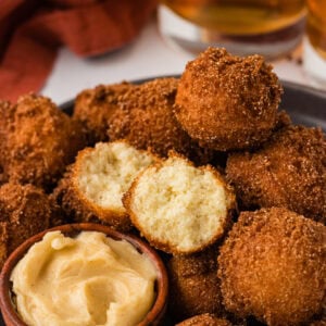 Gluten free hush puppies piled on a plate with one split open showing the soft center, served with honey butter.