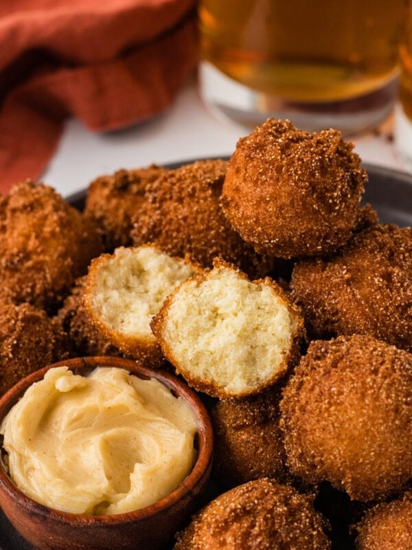 Gluten free hush puppies piled on a plate with one split open showing the soft center, served with honey butter.