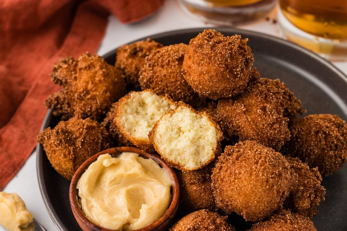 Close up of crispy gluten free hush puppies with honey butter and one broken open to show texture.