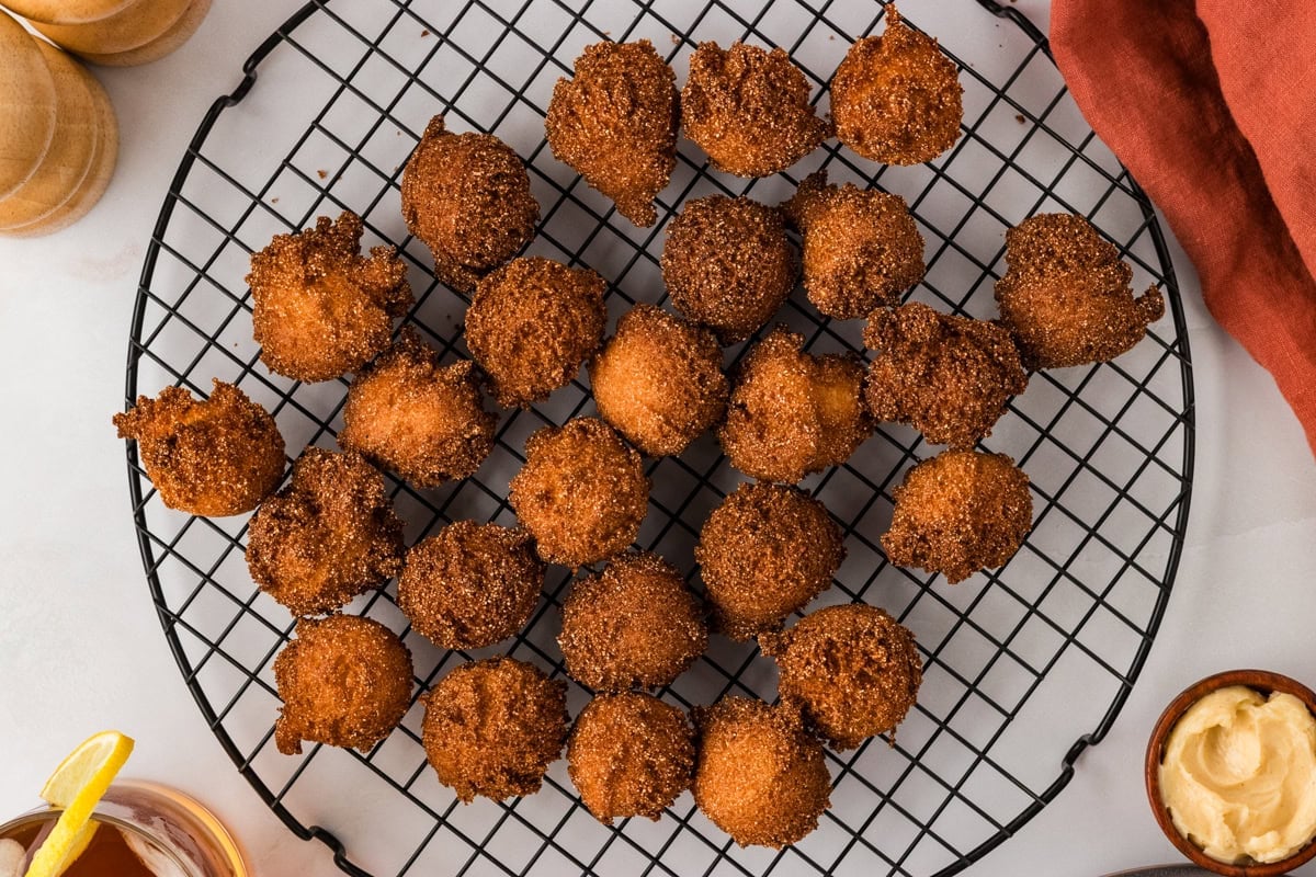 Gluten free hush puppies arranged on a cooling rack with dipping sauce nearby.