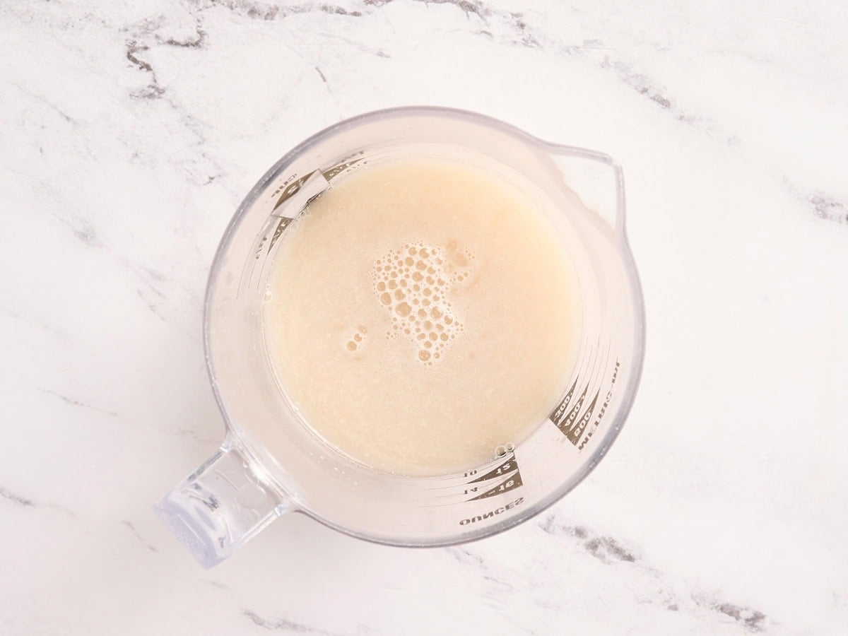 Bloomed yeast mixture in a measuring cup for gluten free challah bread dough.