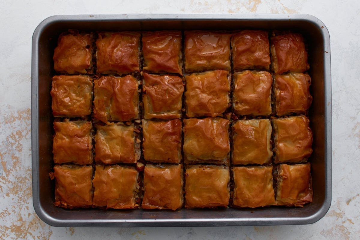 Hot baked gluten-free baklava in a pan after pouring honey syrup over the top.