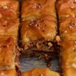 Gluten-free baklava cut into squares showing flaky phyllo layers and chopped nut filling soaked in honey syrup.