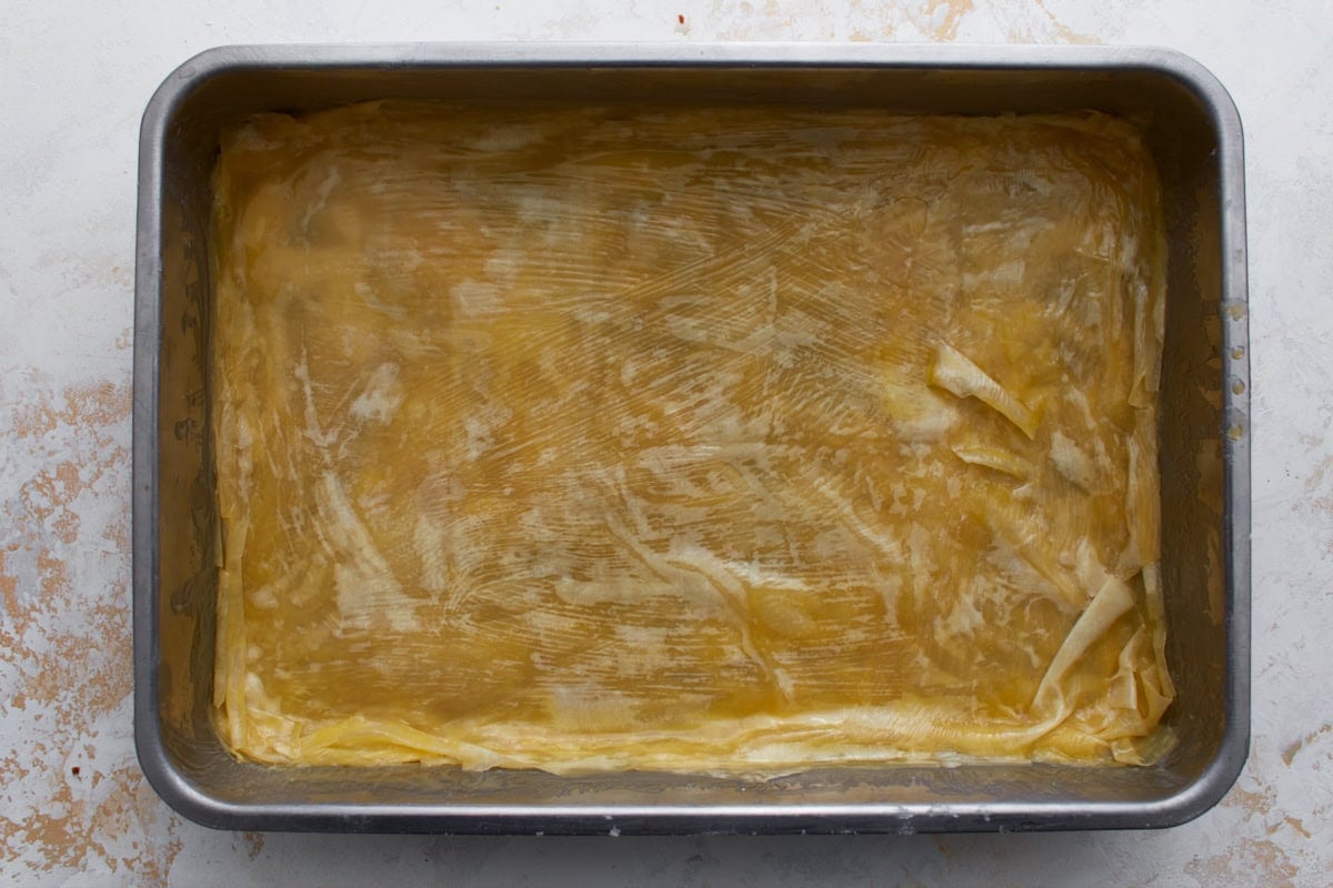 Butter-brushed gluten-free phyllo dough layered in a baking dish for homemade baklava.