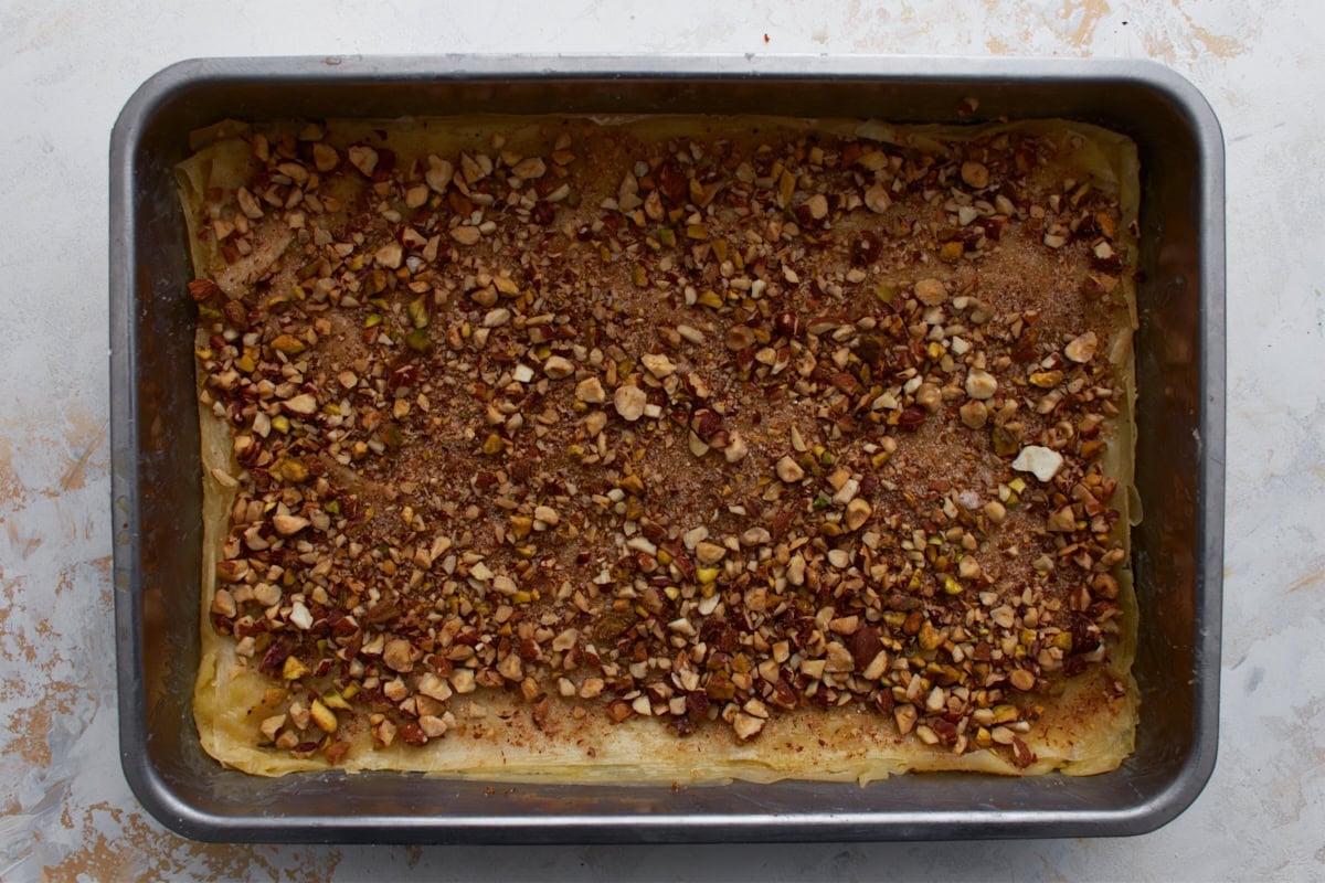 Chopped nut mixture sprinkled over buttered gluten-free phyllo dough in a baking pan.