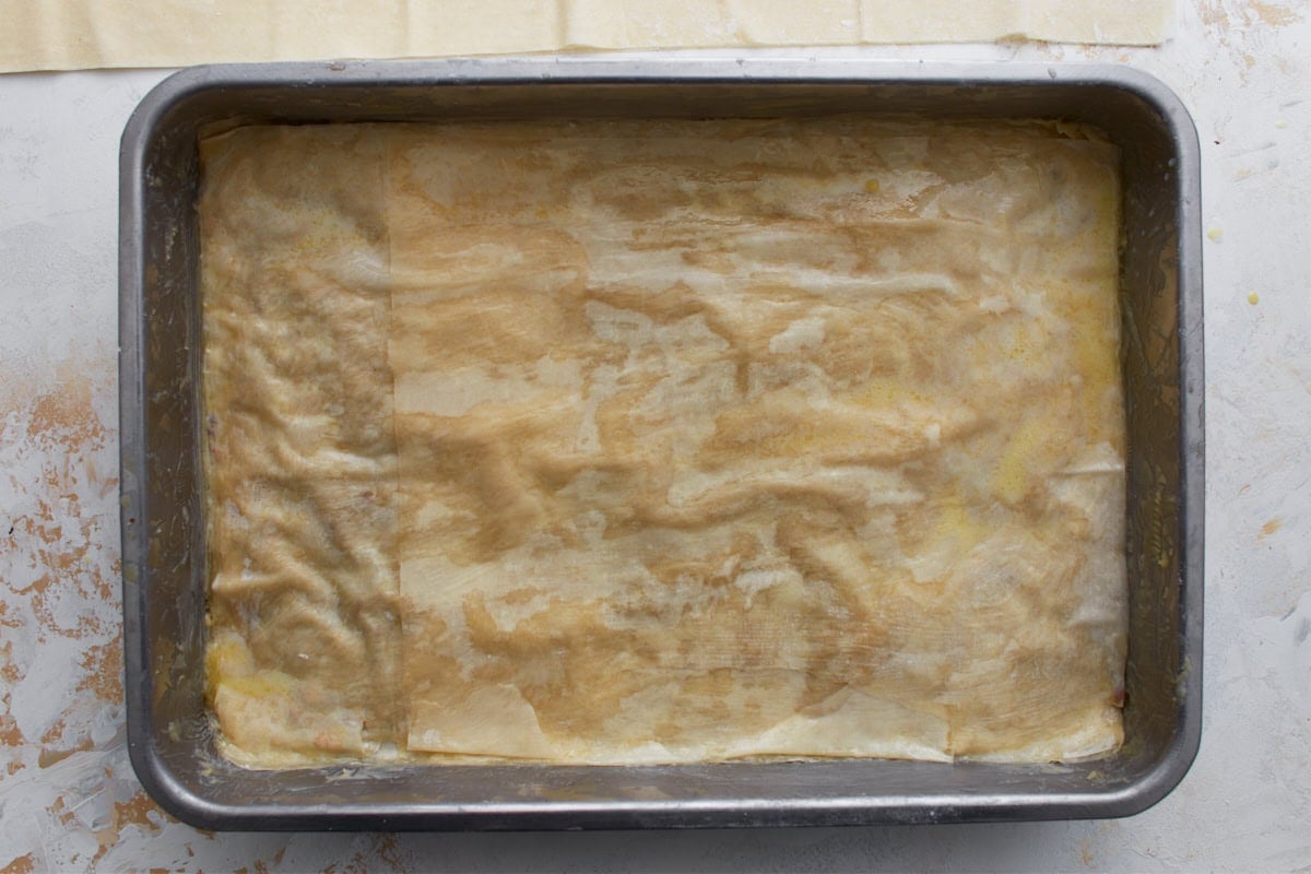 More buttered gluten-free phyllo sheets layered over the nut filling in a baking dish.