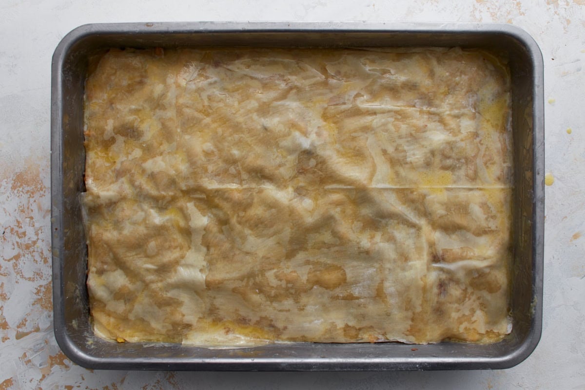 Final layer of butter-brushed gluten-free phyllo dough covering the baklava before baking.