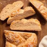 Gluten free challah bread sliced on a wooden board with sesame seeds showing the soft interior crumb.